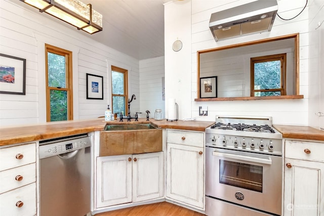 kitchen featuring wood walls, appliances with stainless steel finishes, butcher block countertops, white cabinets, and sink