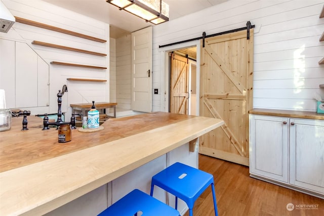 kitchen with wood walls, a barn door, light hardwood / wood-style floors, and a breakfast bar area