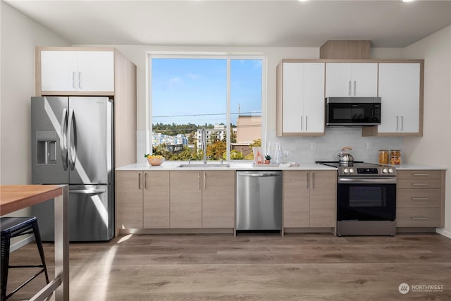 kitchen with white cabinets, sink, decorative backsplash, appliances with stainless steel finishes, and light hardwood / wood-style floors