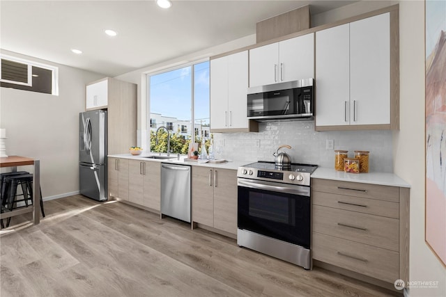 kitchen featuring tasteful backsplash, stainless steel appliances, sink, light hardwood / wood-style flooring, and white cabinets