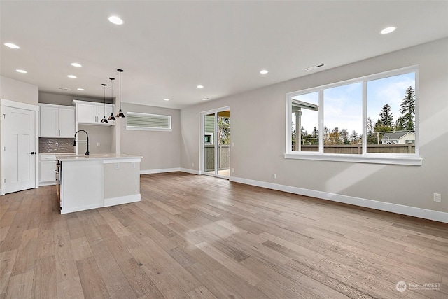 kitchen with white cabinetry, an island with sink, pendant lighting, decorative backsplash, and light wood-type flooring