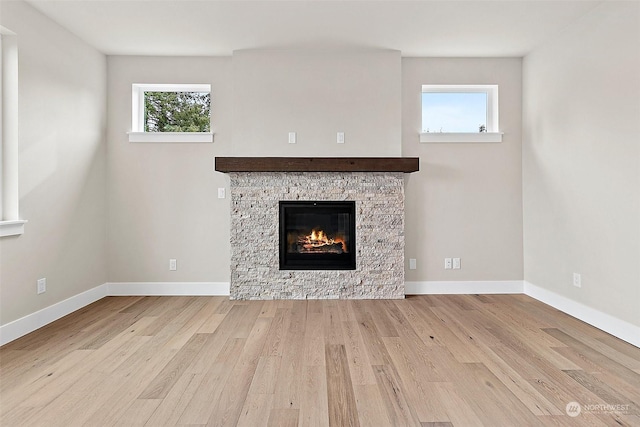 unfurnished living room with light hardwood / wood-style flooring, a stone fireplace, and a healthy amount of sunlight