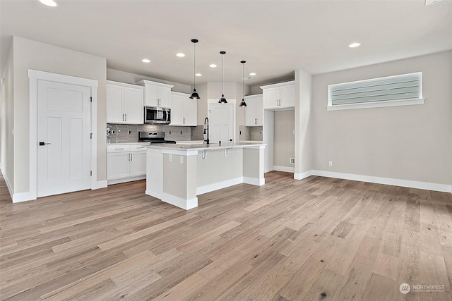 kitchen with white cabinets, pendant lighting, an island with sink, and appliances with stainless steel finishes