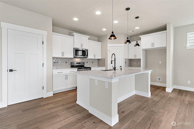 kitchen with white cabinets, appliances with stainless steel finishes, a kitchen island with sink, and sink