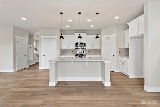 kitchen with white cabinets, pendant lighting, a center island with sink, and stainless steel appliances