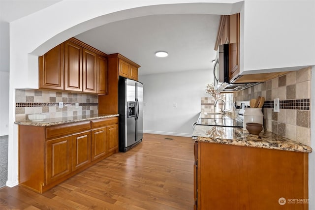 kitchen with sink, light stone counters, light wood-type flooring, stainless steel appliances, and decorative backsplash