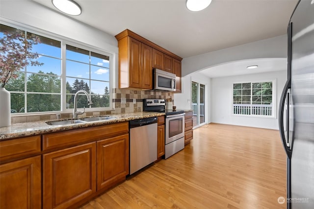 kitchen featuring sink, light hardwood / wood-style flooring, stainless steel appliances, light stone countertops, and decorative backsplash