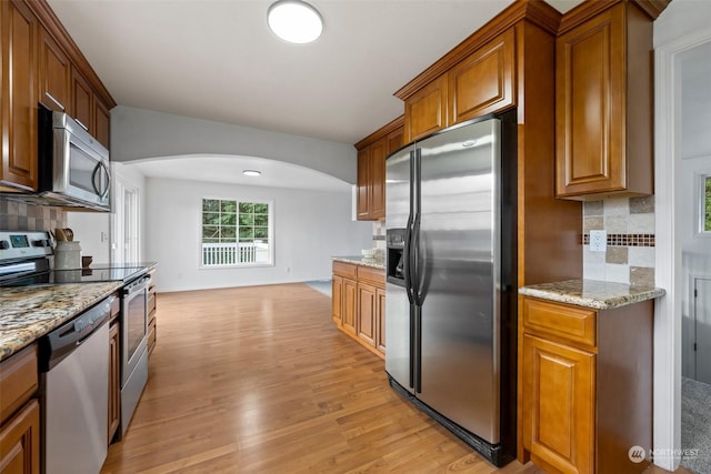 kitchen with tasteful backsplash, light stone countertops, appliances with stainless steel finishes, and light wood-type flooring