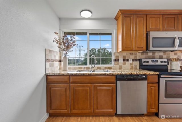 kitchen featuring sink, light hardwood / wood-style flooring, appliances with stainless steel finishes, backsplash, and light stone countertops