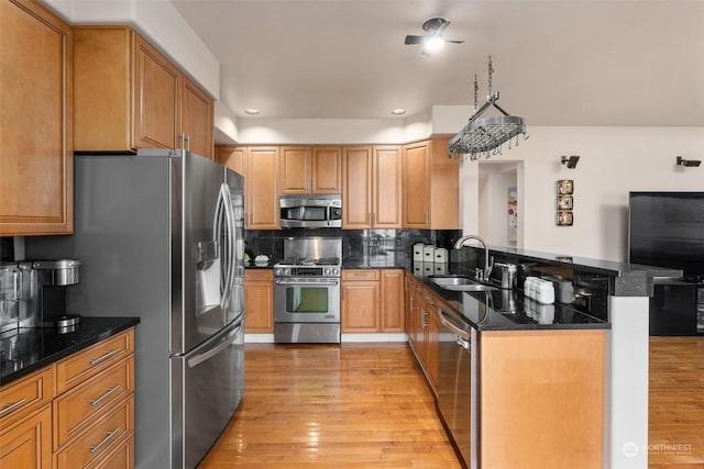 kitchen featuring kitchen peninsula, stainless steel appliances, backsplash, dark stone countertops, and sink