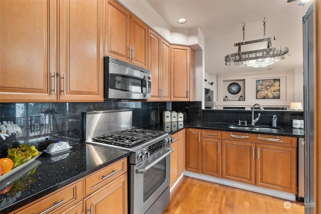 kitchen with tasteful backsplash, dark stone countertops, sink, light wood-type flooring, and appliances with stainless steel finishes