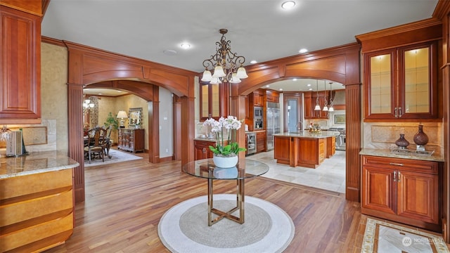 interior space with pendant lighting, a center island, an inviting chandelier, ornate columns, and light stone counters