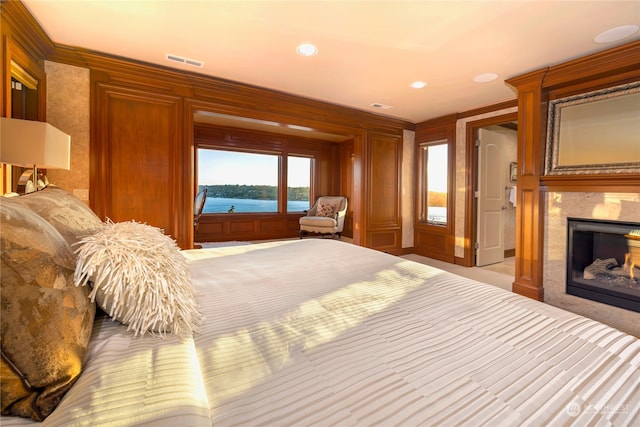 bedroom with a fireplace, a water view, ornamental molding, and wood walls