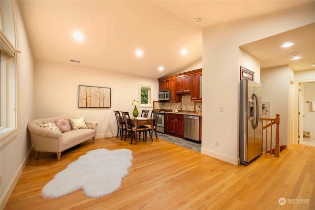 kitchen featuring lofted ceiling, sink, decorative backsplash, light wood-type flooring, and stainless steel appliances