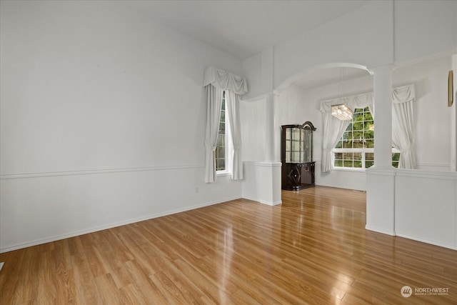 unfurnished room with a notable chandelier, decorative columns, and light hardwood / wood-style flooring