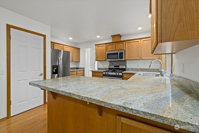 kitchen with light stone counters, sink, kitchen peninsula, and stainless steel appliances