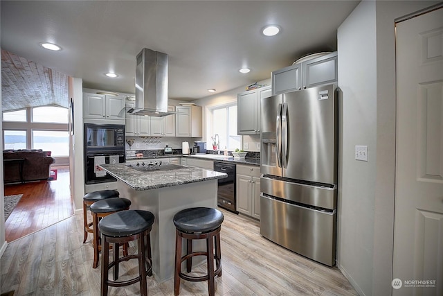 kitchen with a kitchen breakfast bar, island range hood, sink, black appliances, and a center island