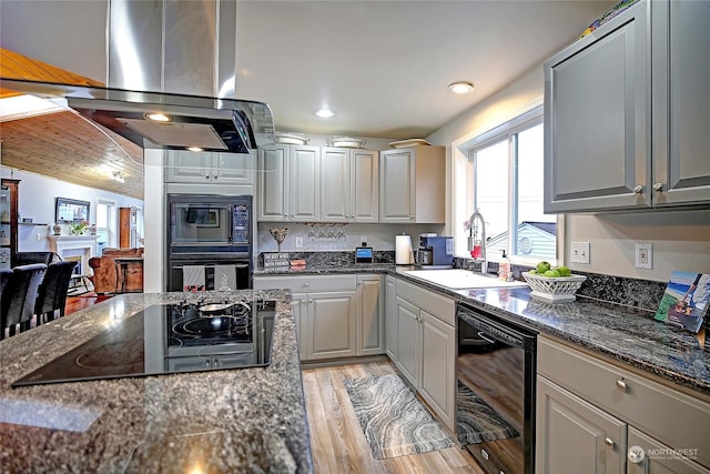 kitchen with sink, dark stone countertops, gray cabinets, island range hood, and black appliances