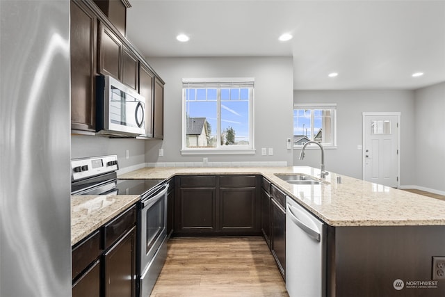 kitchen with sink, light hardwood / wood-style flooring, light stone countertops, kitchen peninsula, and stainless steel appliances