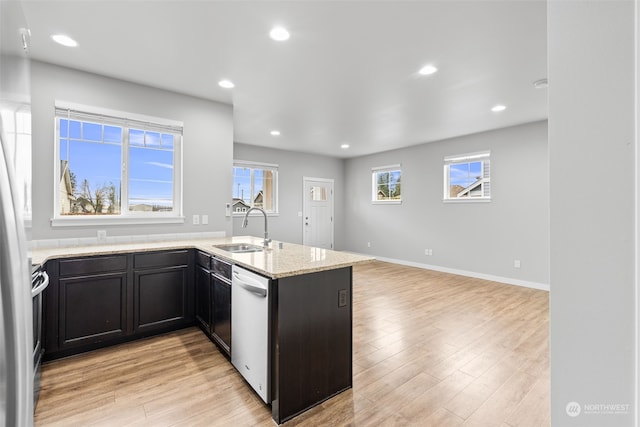 kitchen featuring stainless steel dishwasher, light stone counters, light wood-type flooring, and sink