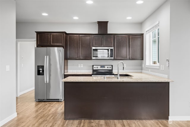 kitchen with sink, light wood-type flooring, appliances with stainless steel finishes, dark brown cabinets, and light stone counters