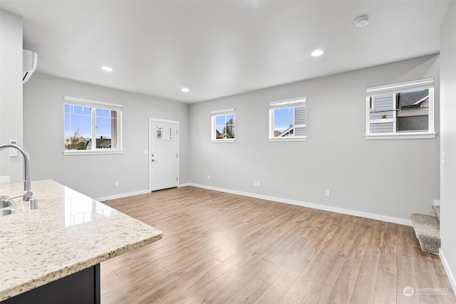 unfurnished living room with light wood-type flooring, sink, and a wall unit AC