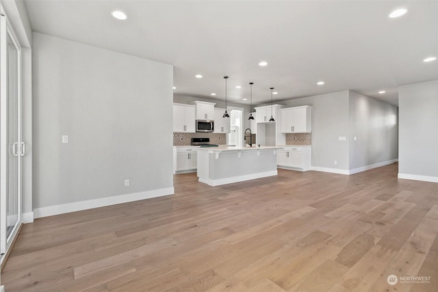 kitchen with white cabinetry, appliances with stainless steel finishes, decorative light fixtures, and a center island with sink