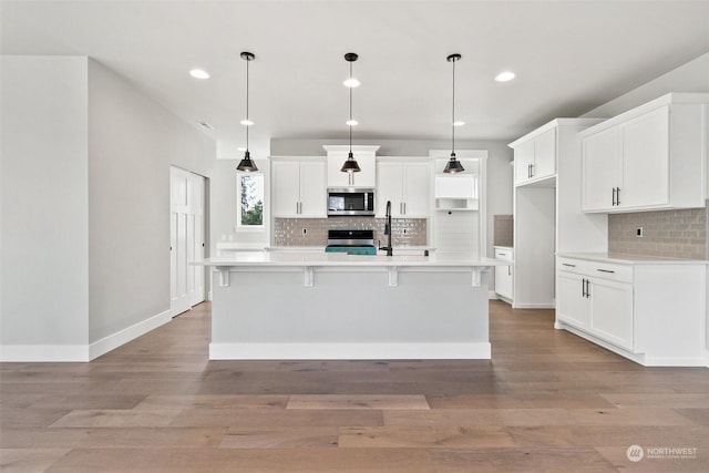 kitchen with stainless steel appliances, an island with sink, and decorative light fixtures