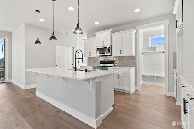 kitchen with appliances with stainless steel finishes, white cabinets, pendant lighting, a kitchen island with sink, and backsplash