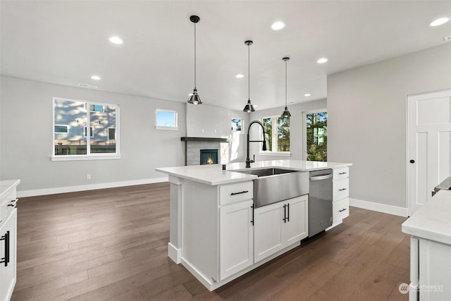 kitchen with decorative light fixtures, white cabinetry, sink, stainless steel dishwasher, and a center island with sink