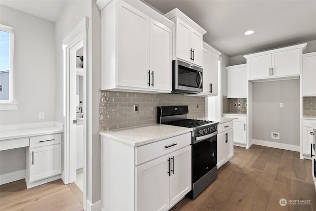 kitchen featuring appliances with stainless steel finishes, tasteful backsplash, white cabinets, light stone counters, and light wood-type flooring