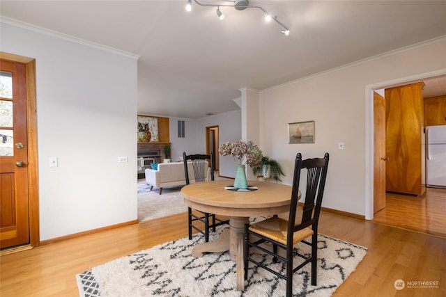 dining space featuring a large fireplace, light wood-type flooring, and crown molding