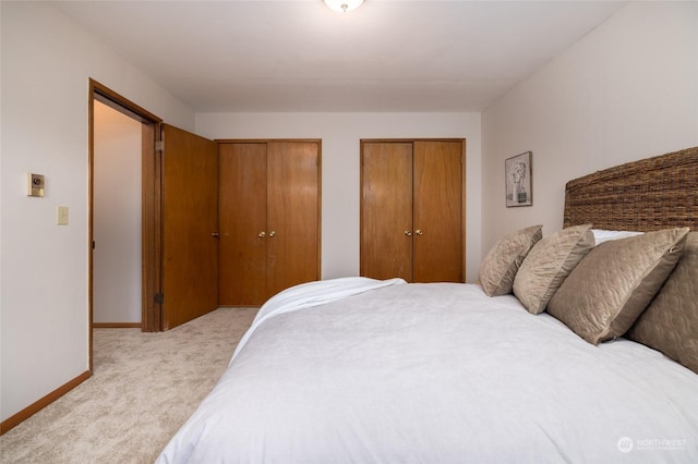 bedroom featuring light colored carpet and multiple closets