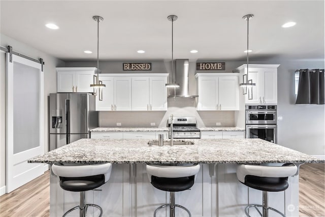 kitchen featuring pendant lighting, wall chimney exhaust hood, stainless steel appliances, and white cabinets