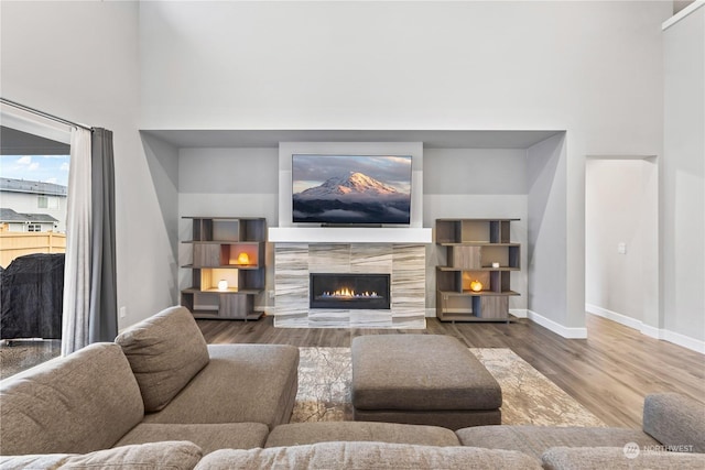 living room featuring a towering ceiling, wood-type flooring, and a tile fireplace