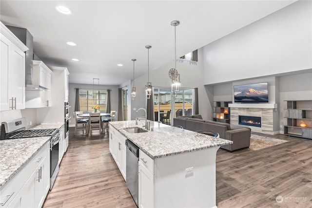 kitchen featuring sink, white cabinetry, hanging light fixtures, stainless steel appliances, and a center island with sink