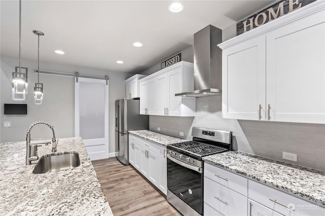 kitchen with wall chimney range hood, sink, appliances with stainless steel finishes, white cabinets, and a barn door