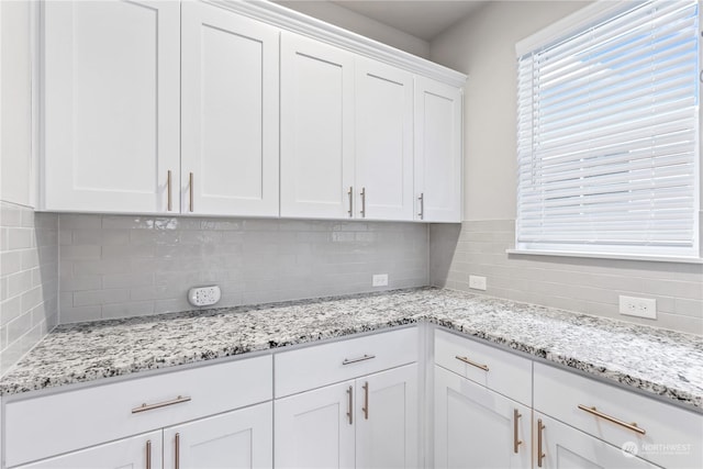 kitchen featuring decorative backsplash, light stone countertops, and white cabinets