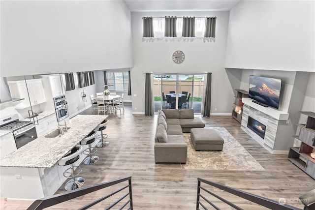 living room with a towering ceiling, light hardwood / wood-style floors, sink, and a tile fireplace