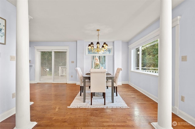 dining space with wood-type flooring, ornate columns, and a notable chandelier