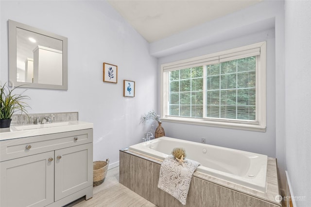 bathroom featuring a relaxing tiled tub, vanity, and vaulted ceiling