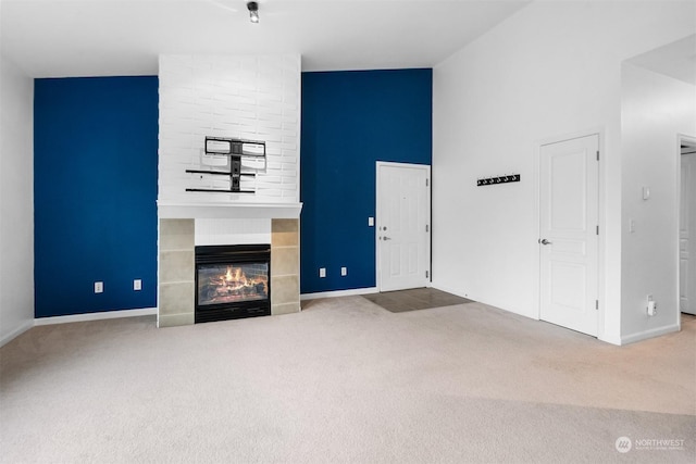 unfurnished living room featuring a tiled fireplace, carpet floors, and high vaulted ceiling