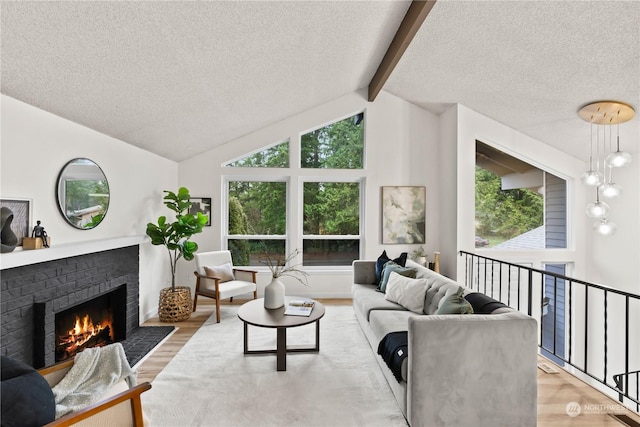 living room featuring vaulted ceiling with beams, a textured ceiling, light hardwood / wood-style floors, and a brick fireplace