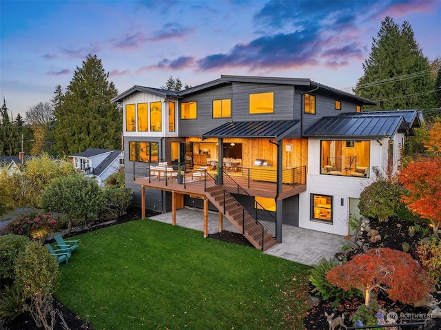 back house at dusk featuring a lawn, a patio, and a deck