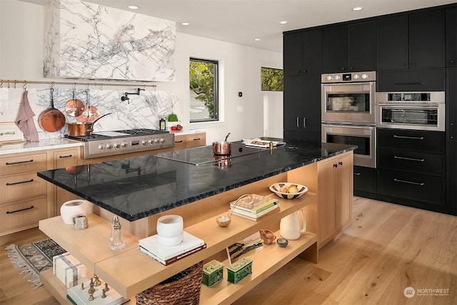 kitchen featuring a center island, light brown cabinets, black electric cooktop, double oven, and light hardwood / wood-style floors