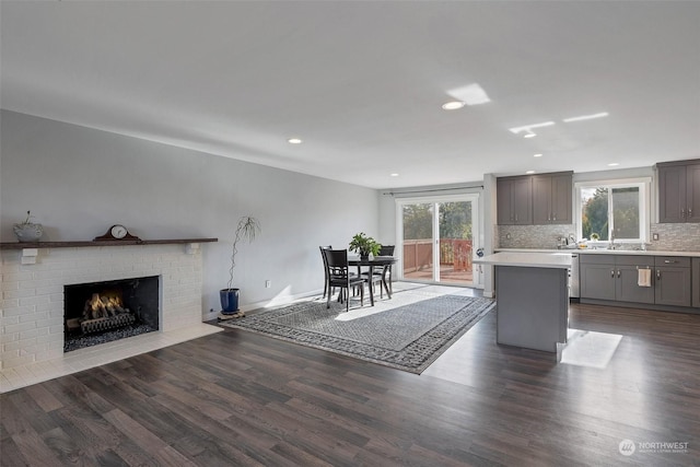 kitchen with decorative backsplash, dark wood-type flooring, sink, a fireplace, and a center island