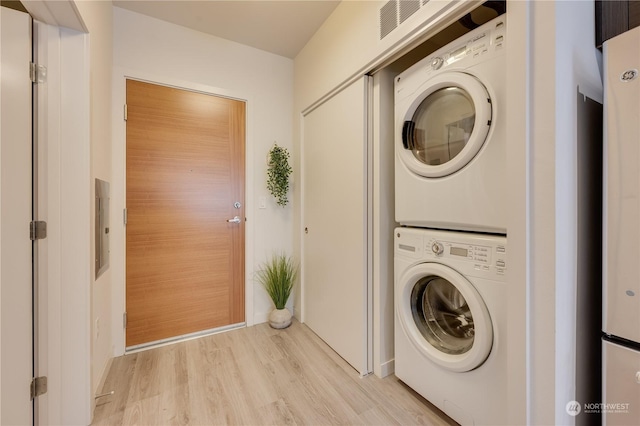 laundry room featuring stacked washing maching and dryer and light hardwood / wood-style flooring