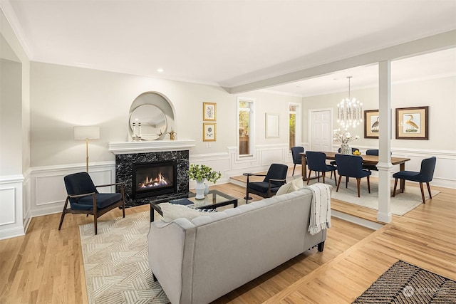 living room with a chandelier, a high end fireplace, light hardwood / wood-style floors, and ornamental molding