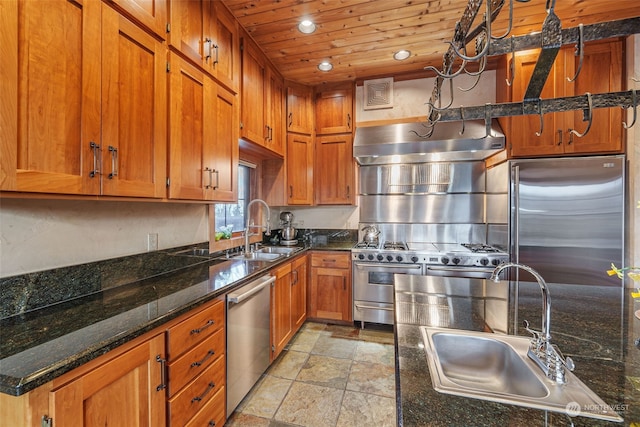 kitchen with high quality appliances, exhaust hood, dark stone countertops, and sink