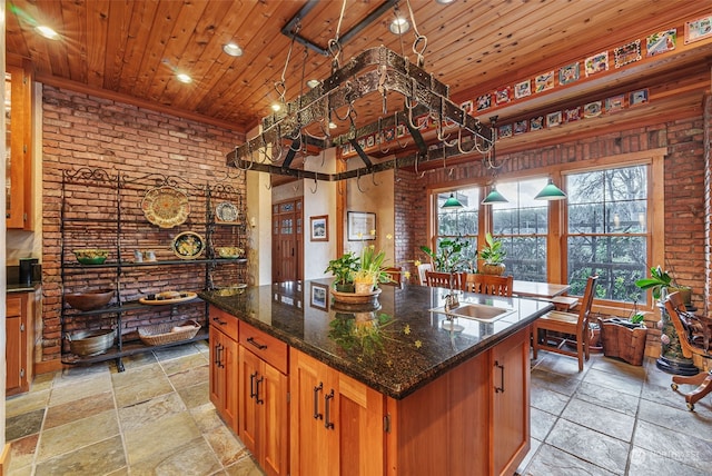 kitchen with dark stone countertops, wooden ceiling, a center island with sink, brick wall, and pendant lighting